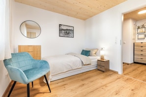 A bedroom with a bed, a chair, a bedside table, a lamp, a mirror, and a picture on the wall.