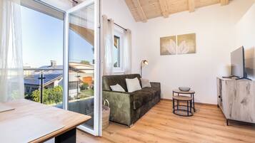 Una sala moderna con un sofá, una mesita, un televisor y un balcón con vistas a paneles solares.