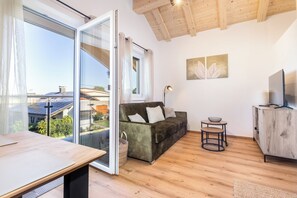 A modern living room with a sofa, a small table, a TV, and a balcony with a view of solar panels.