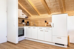 A kitchen with white cabinets, a stainless steel oven, a sink, and wooden ceiling beams.