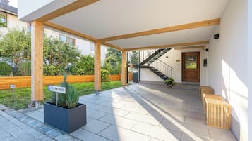 Uma área externa coberta com uma escadaria que leva a uma porta, um vaso com plantas e um banco.