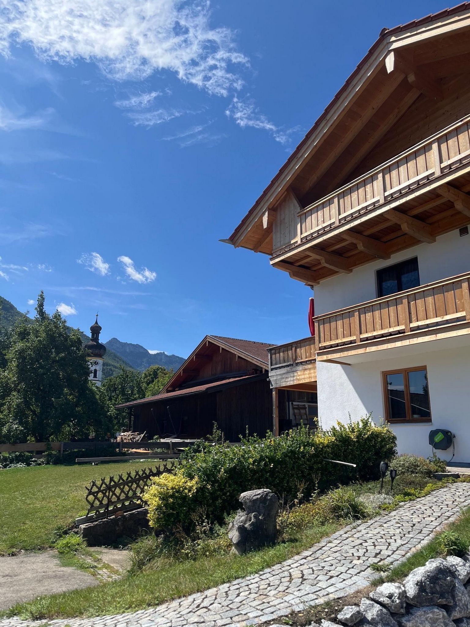 A traditional chalet with a wooden balcony, a stone pathway, and a mountainous backdrop.