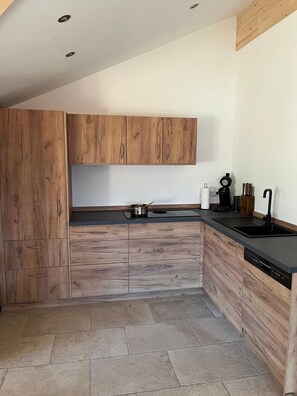 A modern kitchen with wooden cabinets, a black countertop, and a dishwasher. - Hochgern Vacation Rental (Rottau)