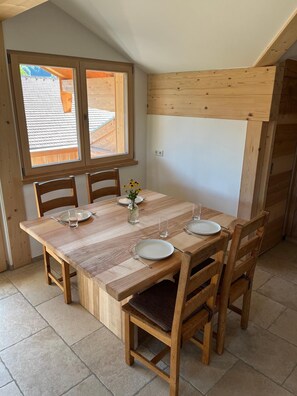A dining area with a wooden table and chairs, a window with a view, and a tiled floor. - Hochgern Vacation Rental (Rottau)
