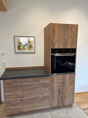 A kitchen with a built-in oven, wooden cabinetry, and a framed artwork on the wall. - Hochgern Vacation Rental (Rottau)
