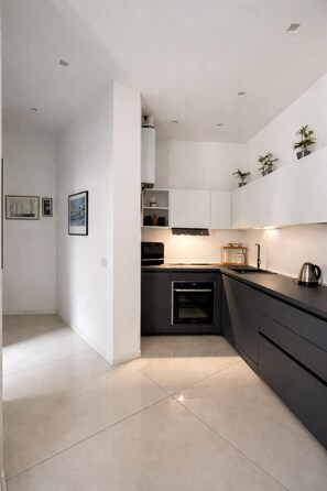 A modern kitchen with dark cabinetry, a built-in oven, and a kettle on the counter. - Peace and Quiet: Designer Apartment in Isola, Prime Location in a Lively Neighborhood (Milano)