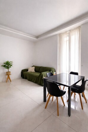 A modern living room with a glass dining table, black chairs, a green sofa, and a potted plant. - Peace and Quiet: Designer Apartment in Isola, Prime Location in a Lively Neighborhood (Milano)