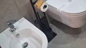 A bathroom with a bidet, toilet, and a wall-mounted flush control panel. - At Vale's House (Pescocostanzo)