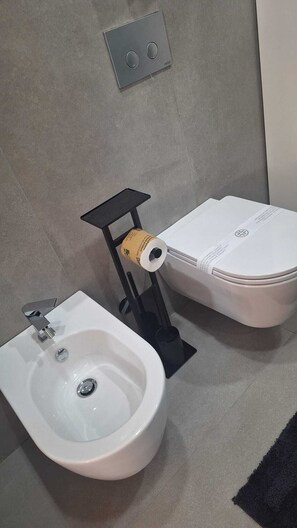 A bathroom with a bidet, toilet, and a wall-mounted flush control panel. - At Vale's House (Pescocostanzo)