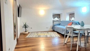A spacious living area with a wooden floor, a sofa, a dining table with chairs, and a small plant. - At Vale's House (Pescocostanzo)