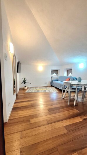 A spacious living area with a wooden floor, a sofa, a dining table with chairs, and a small plant. - At Vale's House (Pescocostanzo)