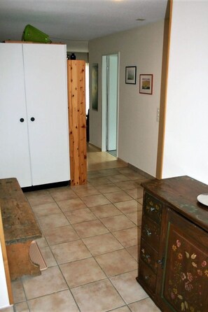 Ein Flur mit einem weißen Kleiderschrank, einer Holztür und einem gefliesten Boden.