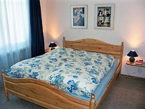 Une chambre à coucher avec un lit en bois, une literie à motifs floraux, deux lampes de chevet et deux tableaux encadrés accrochés au mur.
