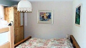 Quarto com beliche, uma cama de solteiro, um guarda-roupa de madeira, um candeeiro de teto branco e um quadro pendurado na parede.