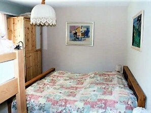 Ein Schlafzimmer mit Etagenbett, einem Einzelbett, einem Holzschrank, einer weißen Deckenleuchte und einem gerahmten Bild an der Wand.