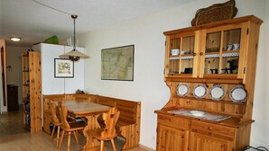 Uma área de refeições com mesa e cadeiras de madeira, um armário com portas de vidro e um lustre.