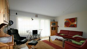Uma sala de estar com um sofá vermelho, uma poltrona de couro preto, um armário de madeira e uma televisão.