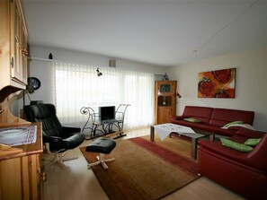 Ein Wohnzimmer mit einem roten Sofa, einem schwarzen Ledersessel, einer Holzkommode und einem Fernseher.