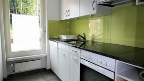 Uma cozinha moderna com armários brancos, bancada preta e uma janela com vista para árvores.