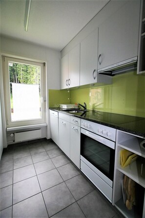 Eine moderne Küche mit weißen Schränken, einer schwarzen Arbeitsplatte und einem Fenster mit Blick auf Bäume.