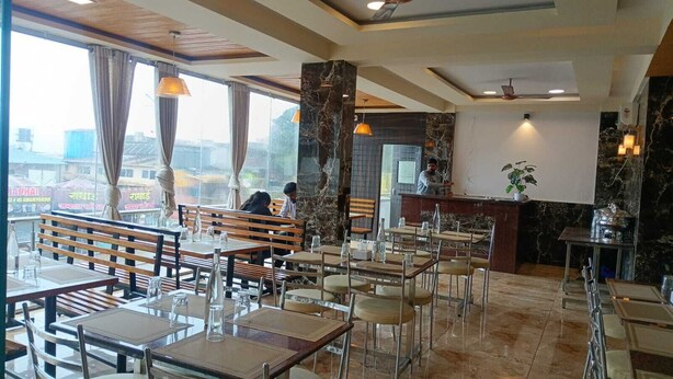 A restaurant interior with wooden benches, tables, and a marble accent wall. - Varo Inn (Mahabaleshwar)