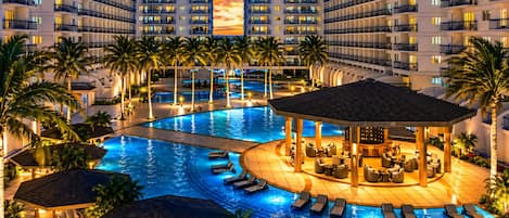 A multi-level hotel with a large indoor swimming pool, lounge areas, and a central bar.