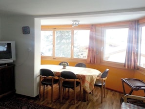 A dining area with a table, chairs, a television, and large windows with curtains. - Gollrad 2 Appartement/Fewo, Dusche, WC, 8-Bettwohnung 7-Bettwohnung/2-Zi-Whg. by Interhome (Arosa)