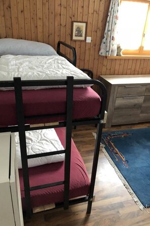A bunk bed with a red mattress, a wooden wall, a small desk, and a window with curtains. - Gollrad 2 Appartement/Fewo, Dusche, WC, 8-Bettwohnung 7-Bettwohnung/2-Zi-Whg. by Interhome (Arosa)