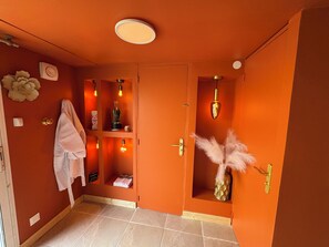 A room with orange walls, a towel hanging on the wall, a shelf with decorative items, and a door with a golden handle.