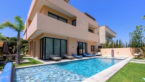 Un edificio moderno a due piani con piscina, area salotto esterna e un giardino curato.