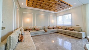 Un ampio soggiorno con un'ampia sezione angolare, un pavimento in marmo lucidato e un design geometrico del soffitto in legno.