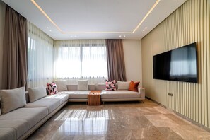 Een moderne woonkamer met een hoekbank, een salontafel en een flatscreen televisie aan de muur.