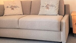 Un divano con due cuscini decorativi, un quadro appeso al muro e un piccolo tavolino in legno.
