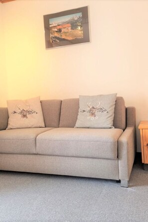 Ein Sofa mit zwei dekorativen Kissen, einem gerahmten Bild an der Wand und einem kleinen Holznachttisch.