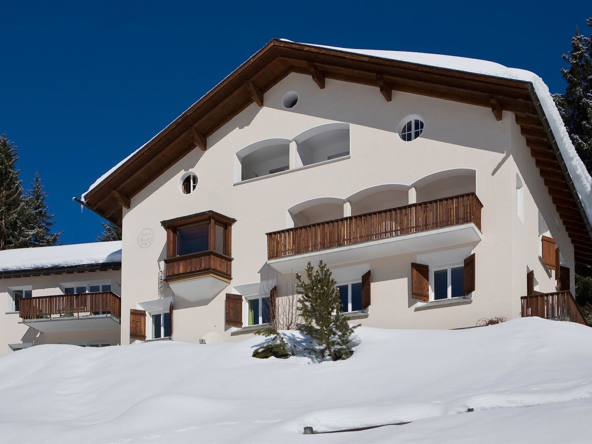 Un edificio de varios pisos con balcones, un techo cubierto de nieve y un cielo azul despejado.