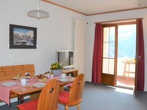 Ein Essbereich mit Tisch für zwei Personen, einem Fernseher und einem Fenster mit Vorhängen.