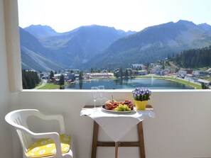 A balcony with a table set for two, overlooking a mountainous landscape with a lake and buildings. - Bisang R Appartement/Fewo,   4-Bettwohnung by Interhome (Arosa)