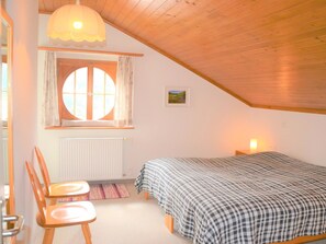 Ein Schlafzimmer mit einem Bett, einem Fenster mit Vorhängen, einer Heizung, einem Stuhl und einer Wandleuchte.