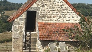 A stone cottage with a chimney, a small door, and two wicker chairs outside.