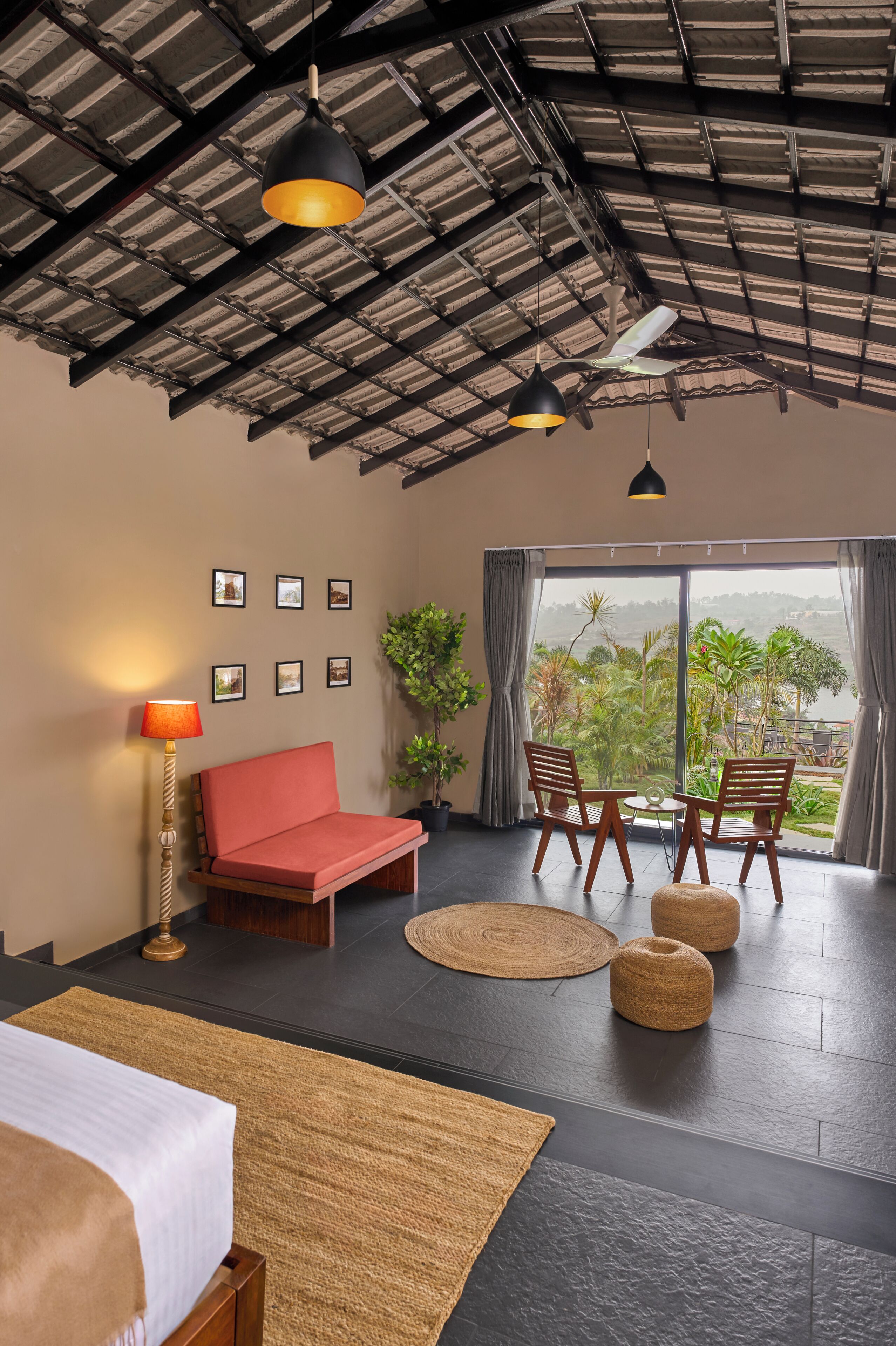 Una habitación moderna con una cama, un sofá rojo, una mesa de comedor con sillas, un ventanal con vistas y un techo con vigas a la vista.