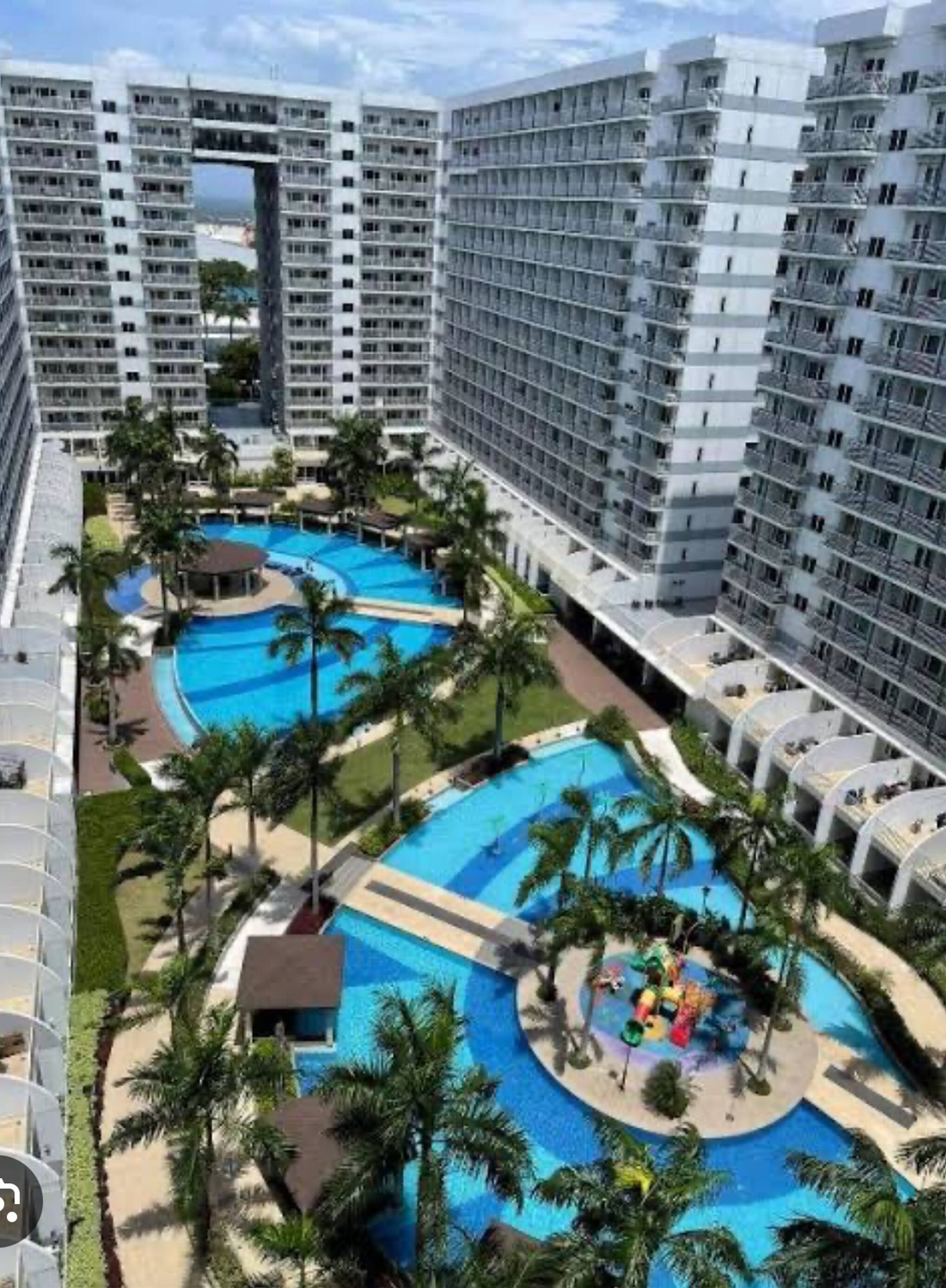 Un hotel de gran altura con varios balcones y una zona de piscina central rodeada de palmeras.