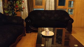 Una habitación con un sofá de color oscuro, una mesa de centro de vidrio y un adorno, además de una planta en maceta con flores rojas.