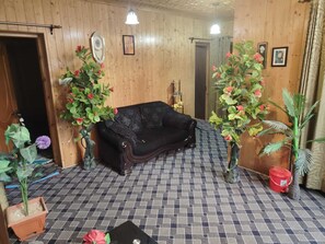 Una habitación con un sofá negro, paredes de madera, piso de baldosas y plantas en macetas.