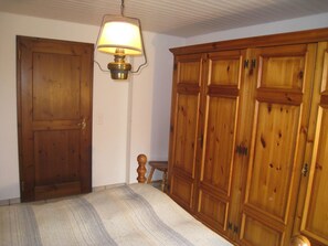 A room with a wooden wardrobe, a bed with a striped blanket, and a wall-mounted lamp. - Casa Laghetto 5 Appartement/Fewo, Bad, WC, 4-Bettwohnung 4-Bettwohnung by Interhome (Arosa)