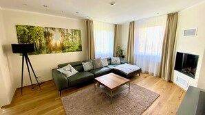 A modern living room with a sectional sofa, a coffee table, a large painting, a floor lamp, and a fireplace. - HarzVilla (Bad Sachsa)