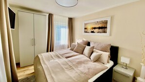 A hotel room with a bed, a nightstand, a lamp, a wardrobe, and a painting on the wall. - HarzVilla (Bad Sachsa)