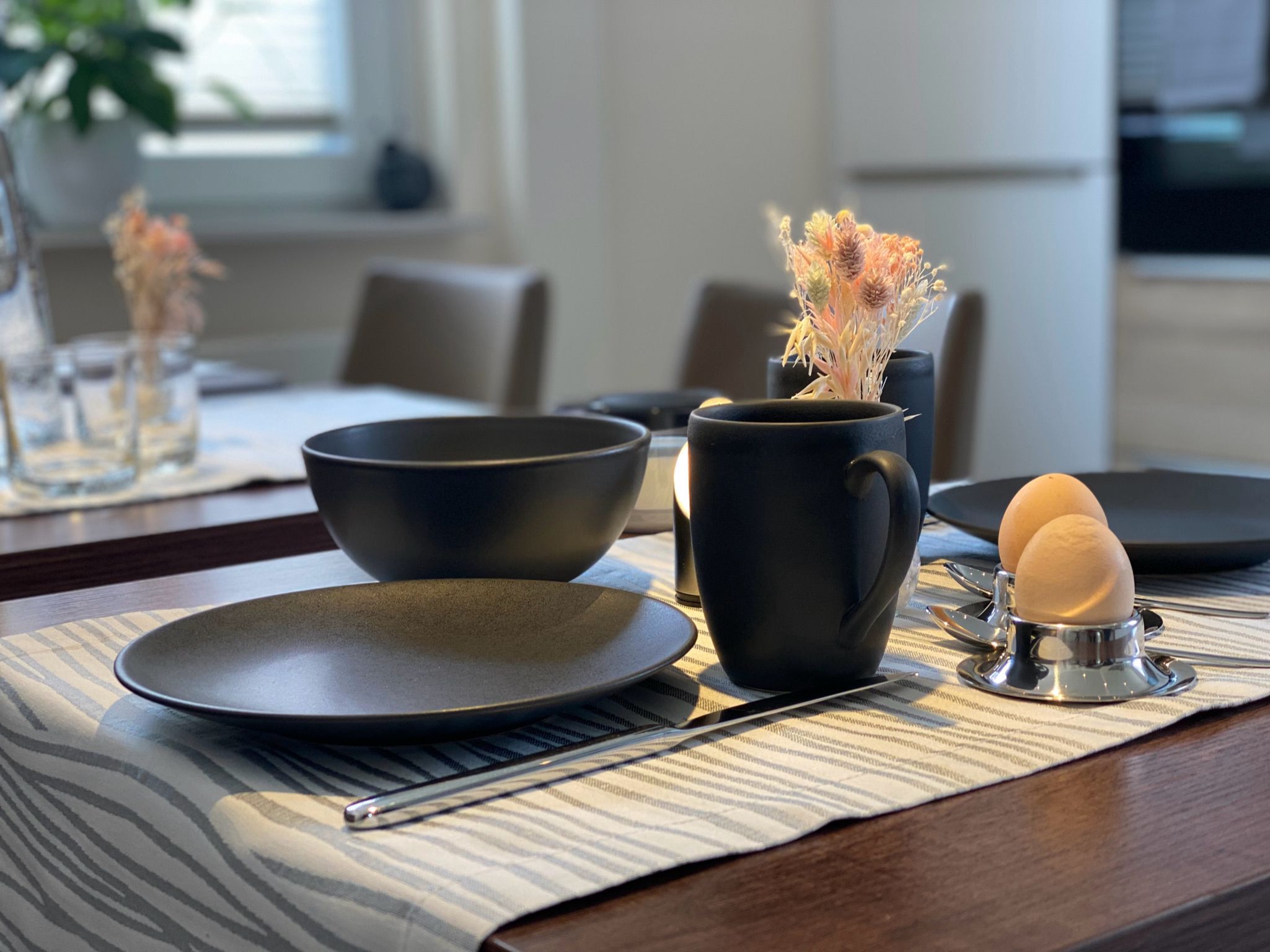 A dining table with a placemat, a black bowl, a black mug, and a stethoscope with an egg.