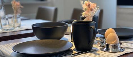 A dining table with a placemat, a black bowl, a black mug, and a stethoscope with an egg.
