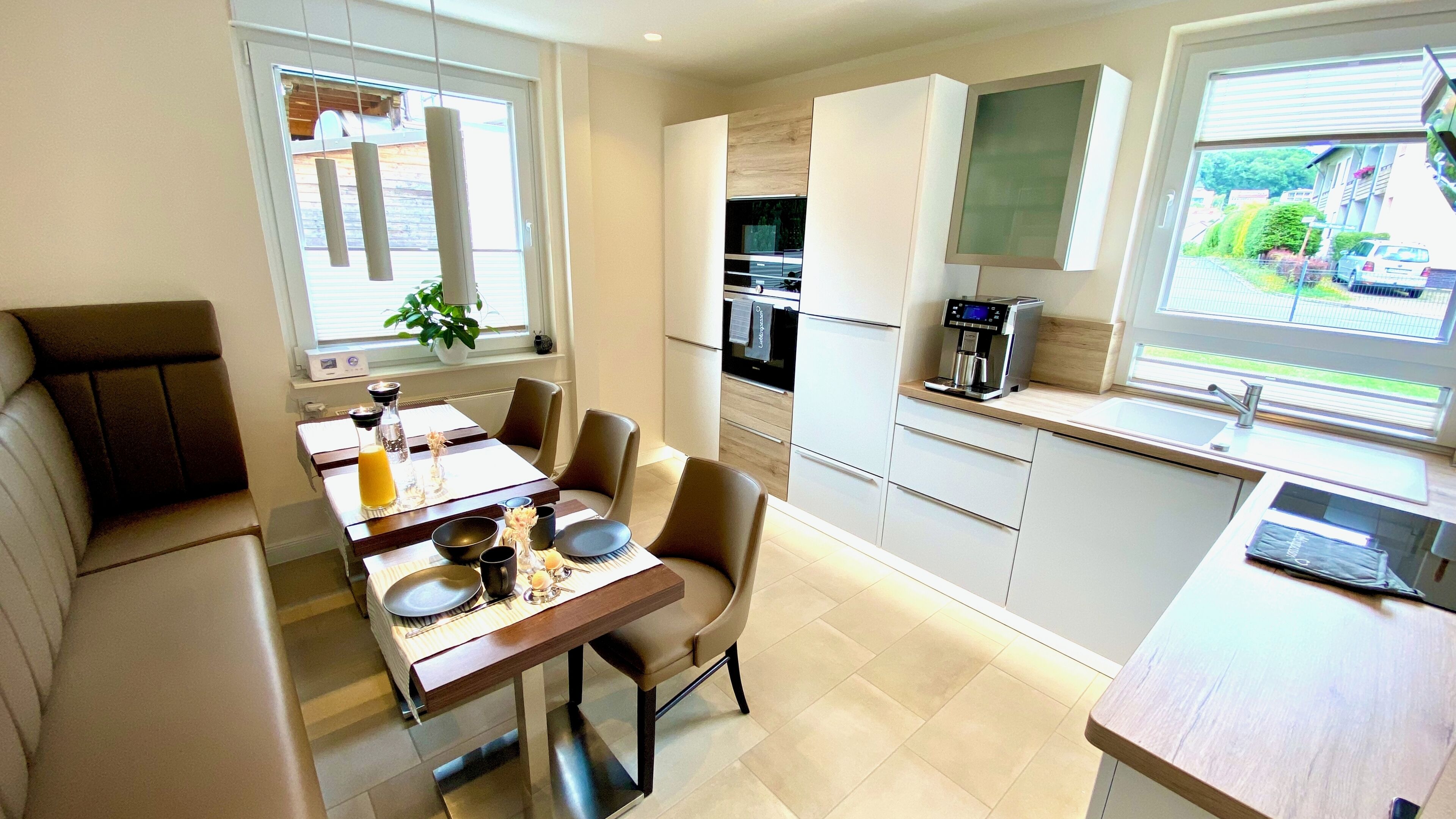 A modern kitchen with a dining area, a coffee machine, and a view of the outside.