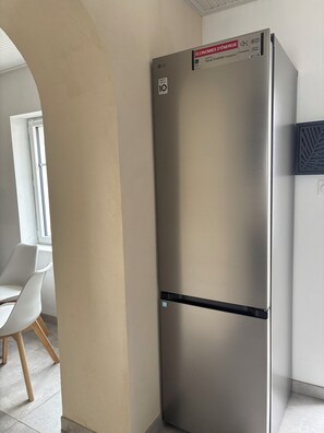 Una cocina moderna con un refrigerador de acero inoxidable, una silla blanca y un ventanal.